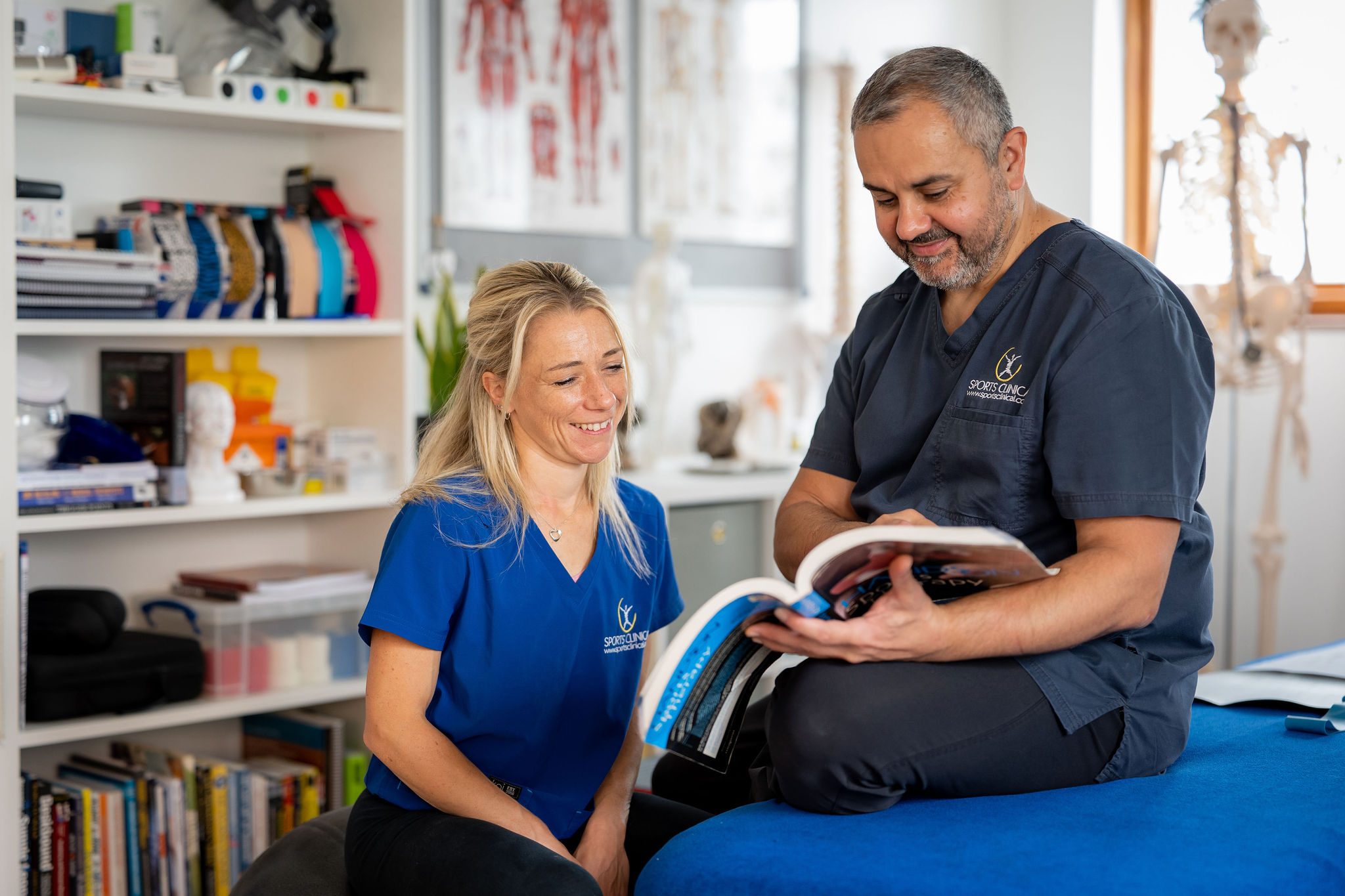 Both SPORTS CLINICAL practitioners together in the clinic, looking through a textbook