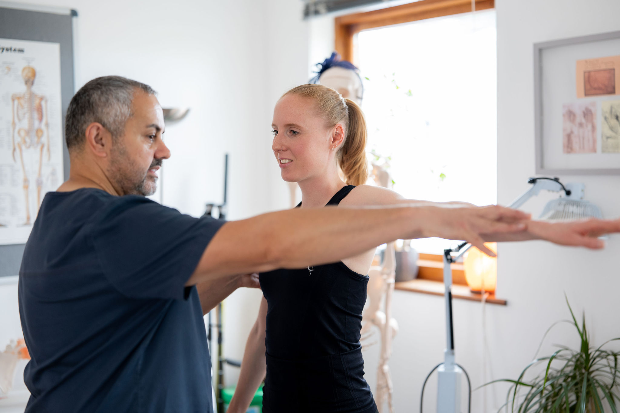 A SPORTS CLINICAL practitioner supporting a patient through a guided shoulder movement in the clinic